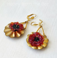 Red Poppy earrings set against brass ribbons