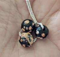Faceted gemstone necklace features pink and black Mexican Red Snowflake Jasper beads and sterling silver chain