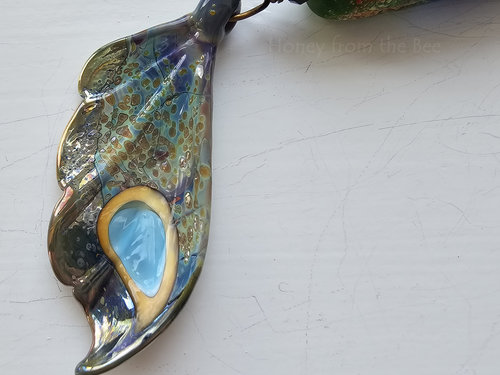 Artisan necklace has a butterfly wing in shades of aqua, yellow, purple