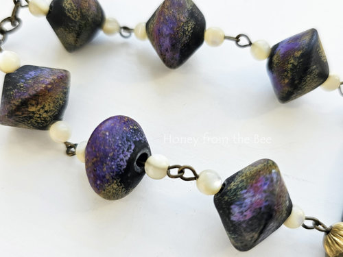 Art necklace features lampwork by Angelica Schott in shades of black, purple and gold.