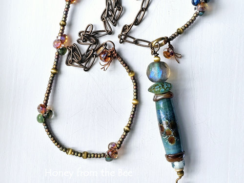 Tunic length art necklace features lampwork in shades of blue green and amber