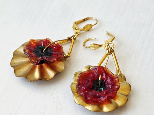 Red Poppy earrings set against brass ribbons