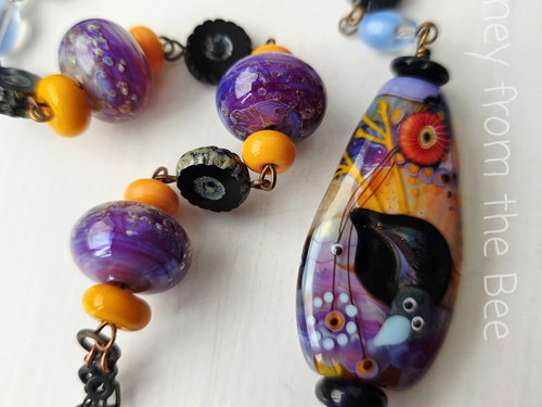 Statement necklace features crow lampwork in purple, orange and blue