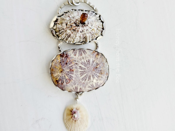 Lavender and cream beach inspired art necklace features fossilized coral agate and two found shells with a faceted tourmaline.