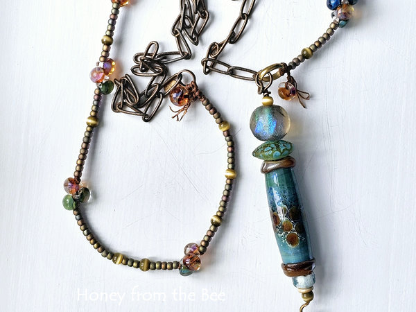 Tunic length art necklace features lampwork in shades of blue green and amber