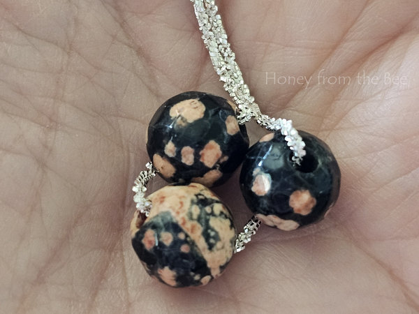 Faceted gemstone necklace features pink and black Mexican Red Snowflake Jasper beads and sterling silver chain